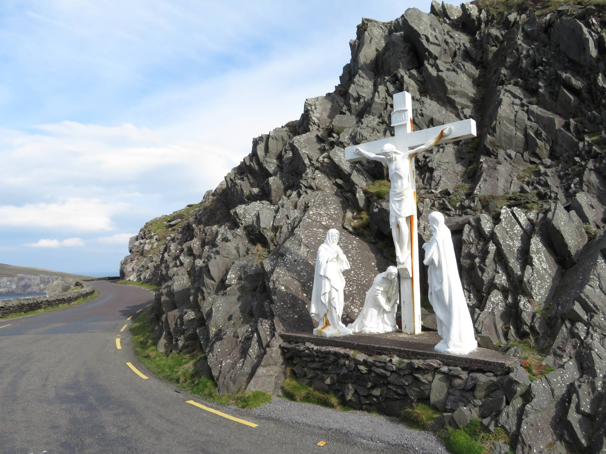 The white Crucifixion cross set into the rock at Slea Head, with the coast road curving away and the Atlantic beyond